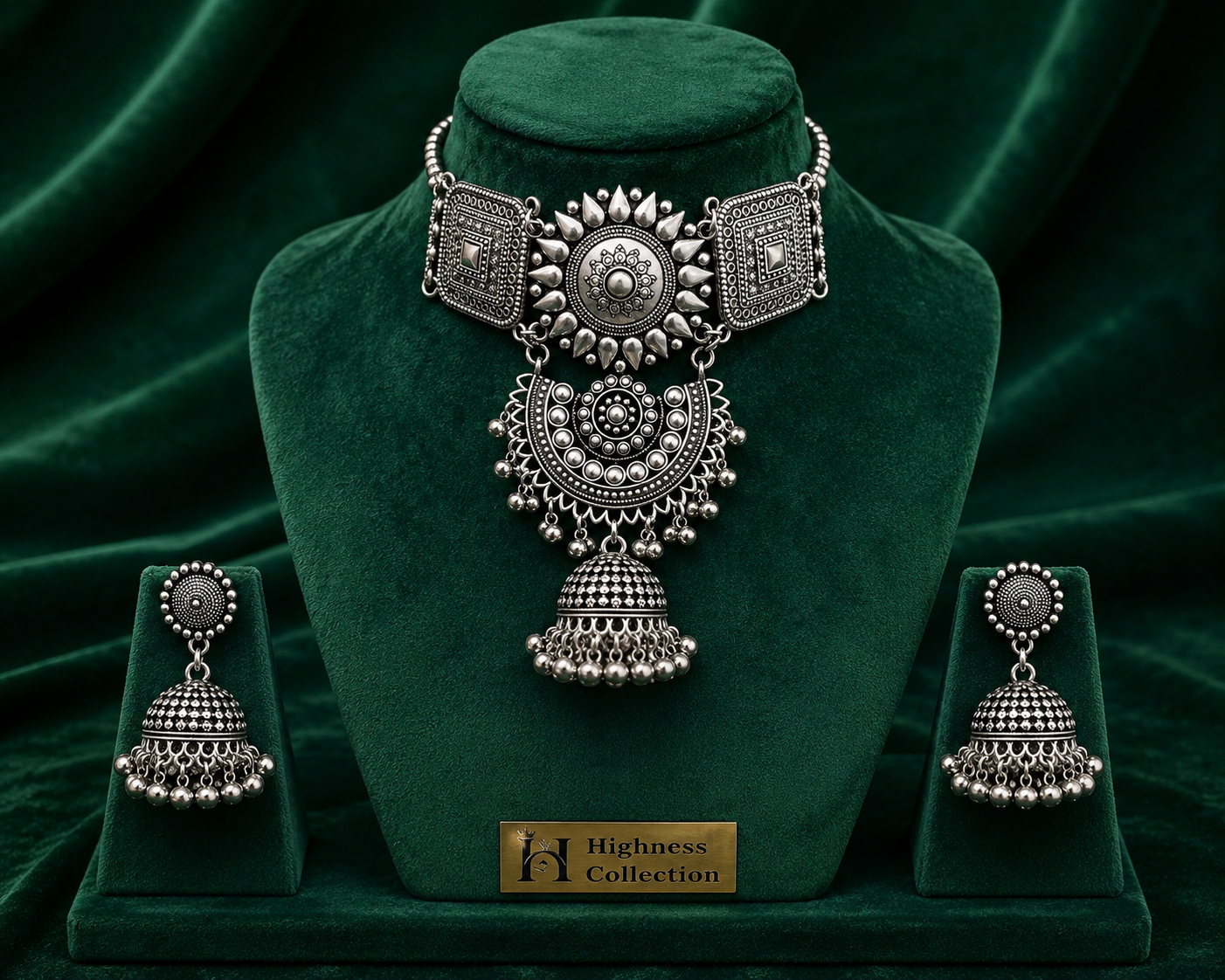 An ornate silver-toned jewelry set displayed on a dark green velvet mannequin bust and matching stands. The set includes a choker necklace with a large central pendant, a matching pair of dangling earrings, and a small gold plaque reading 'Highness Collection'.